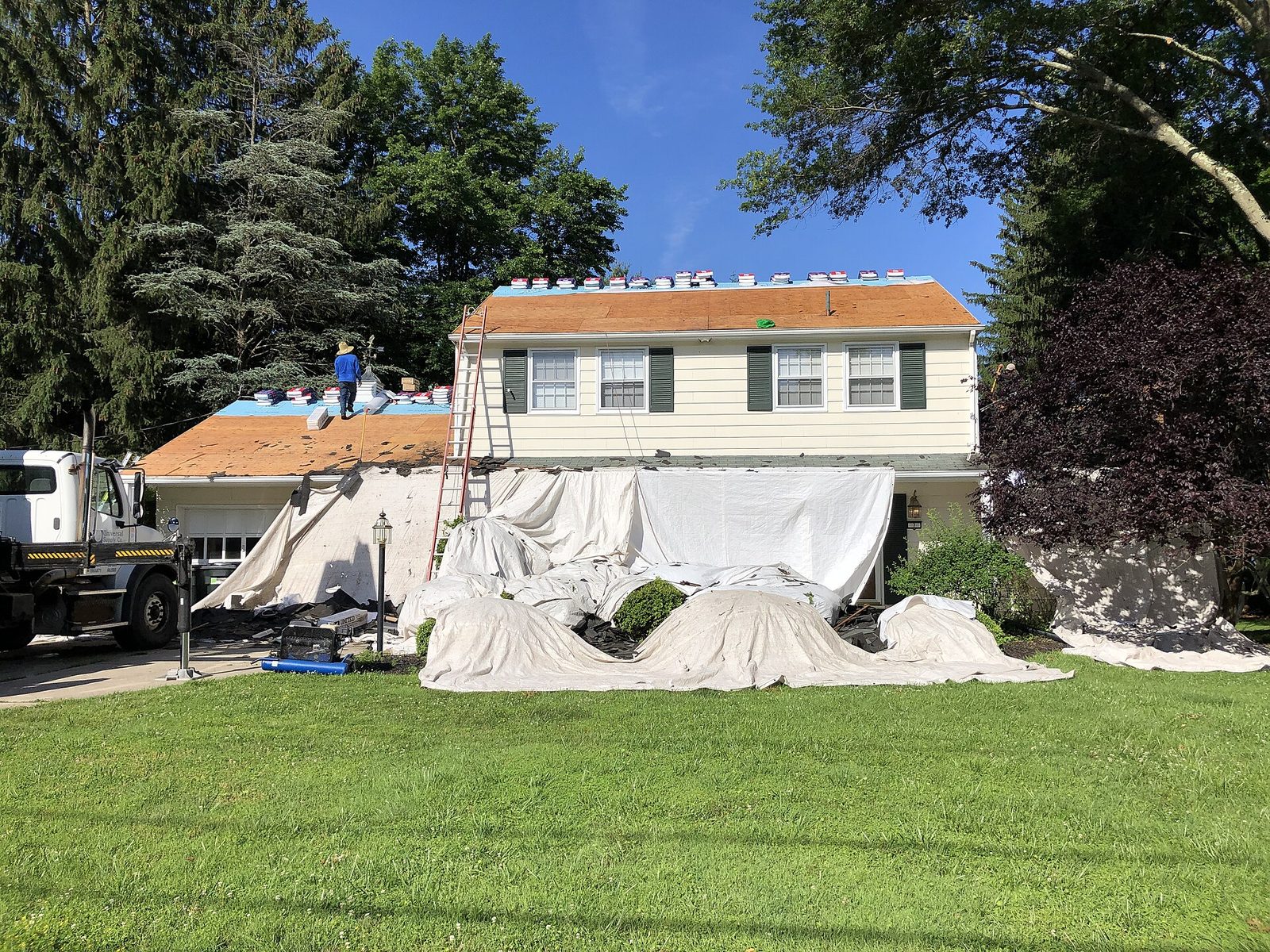 Roofing crew replacing the roof of a suburban house with tarps on the lawn