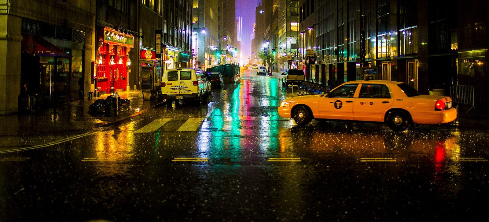 Rain-soaked New York street at night glowing with neon signs and a yellow taxi