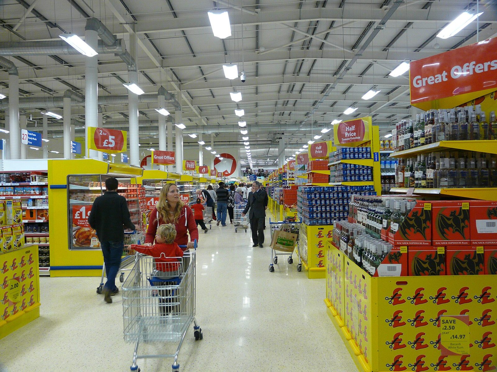 Shoppers with a trolley browsing a brightly lit supermarket aisle
