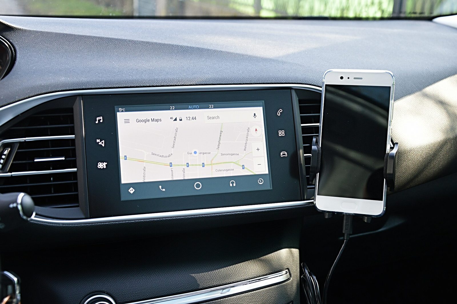 Car dashboard screen showing Google Maps navigation beside a mounted phone