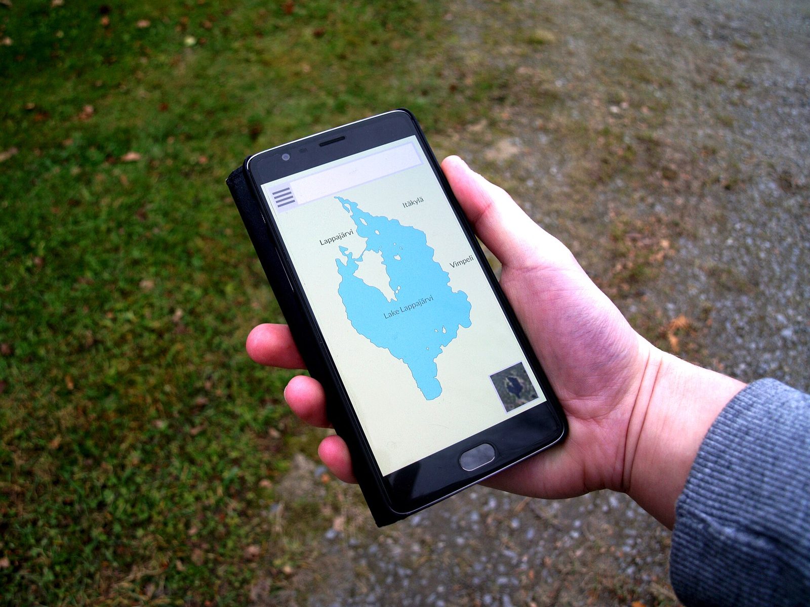 Hand holding a smartphone showing a map app outdoors on a path