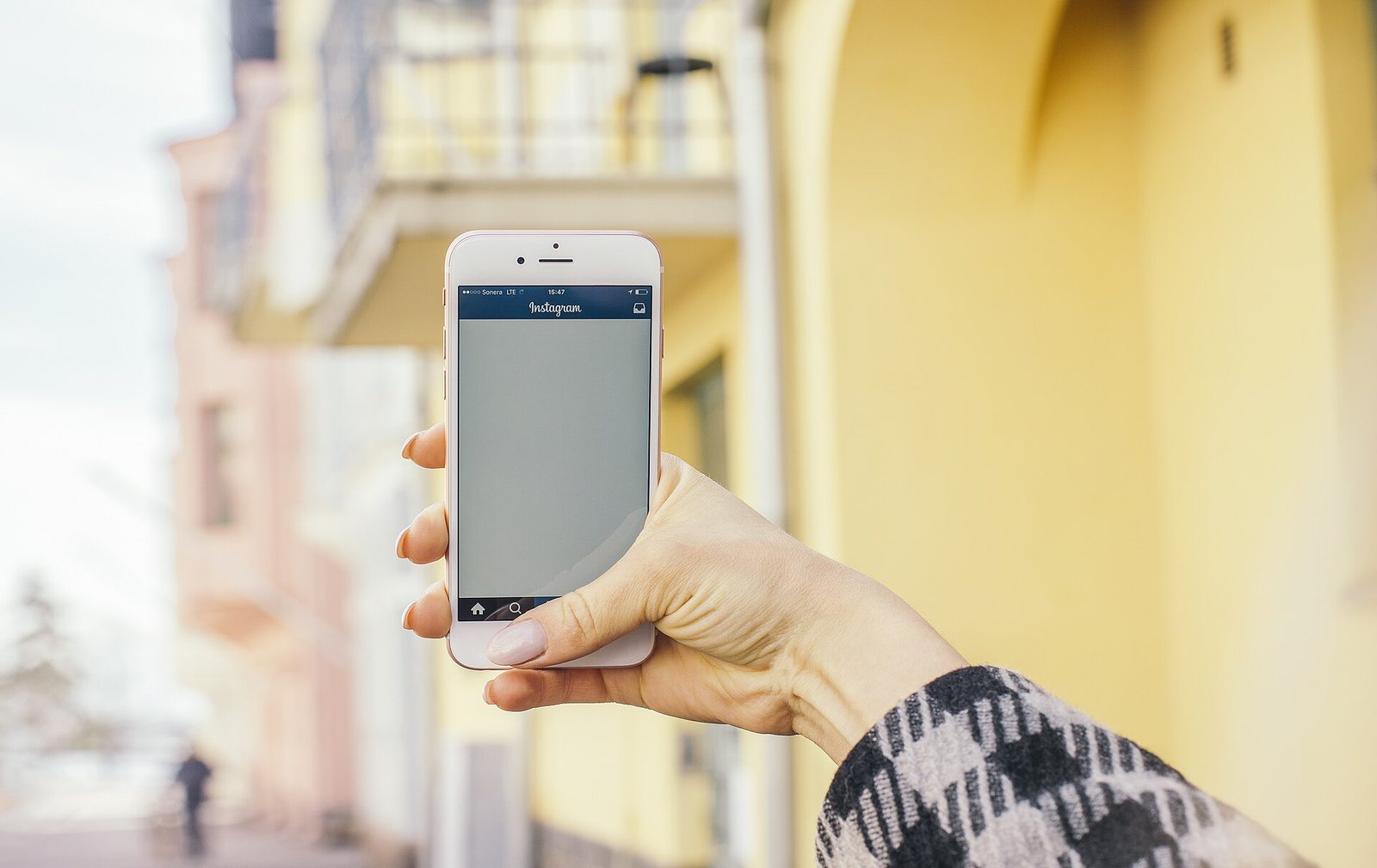 Hand holding a smartphone up on a sunny city street