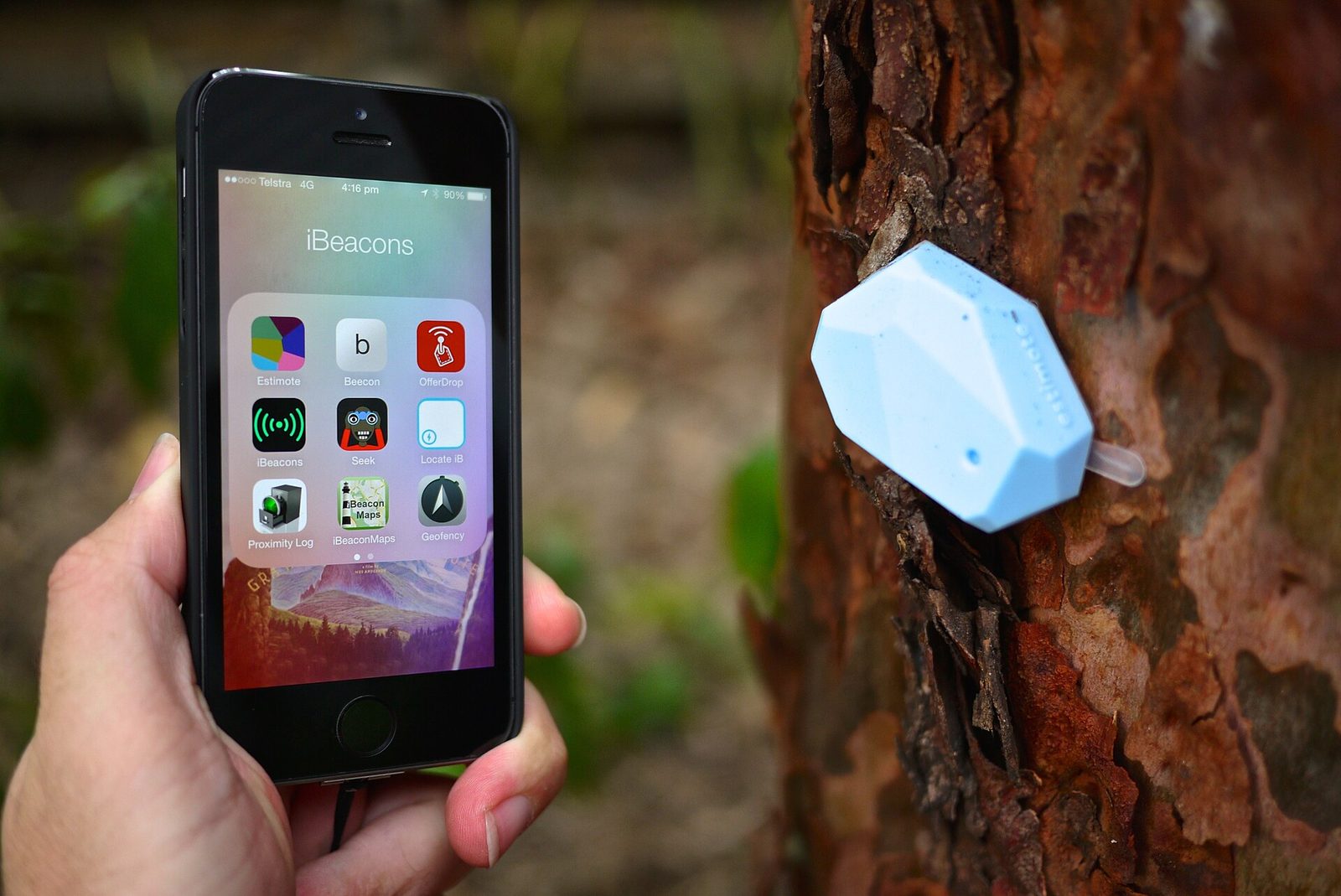 Hand holding a smartphone with a beacon app beside a small Bluetooth beacon