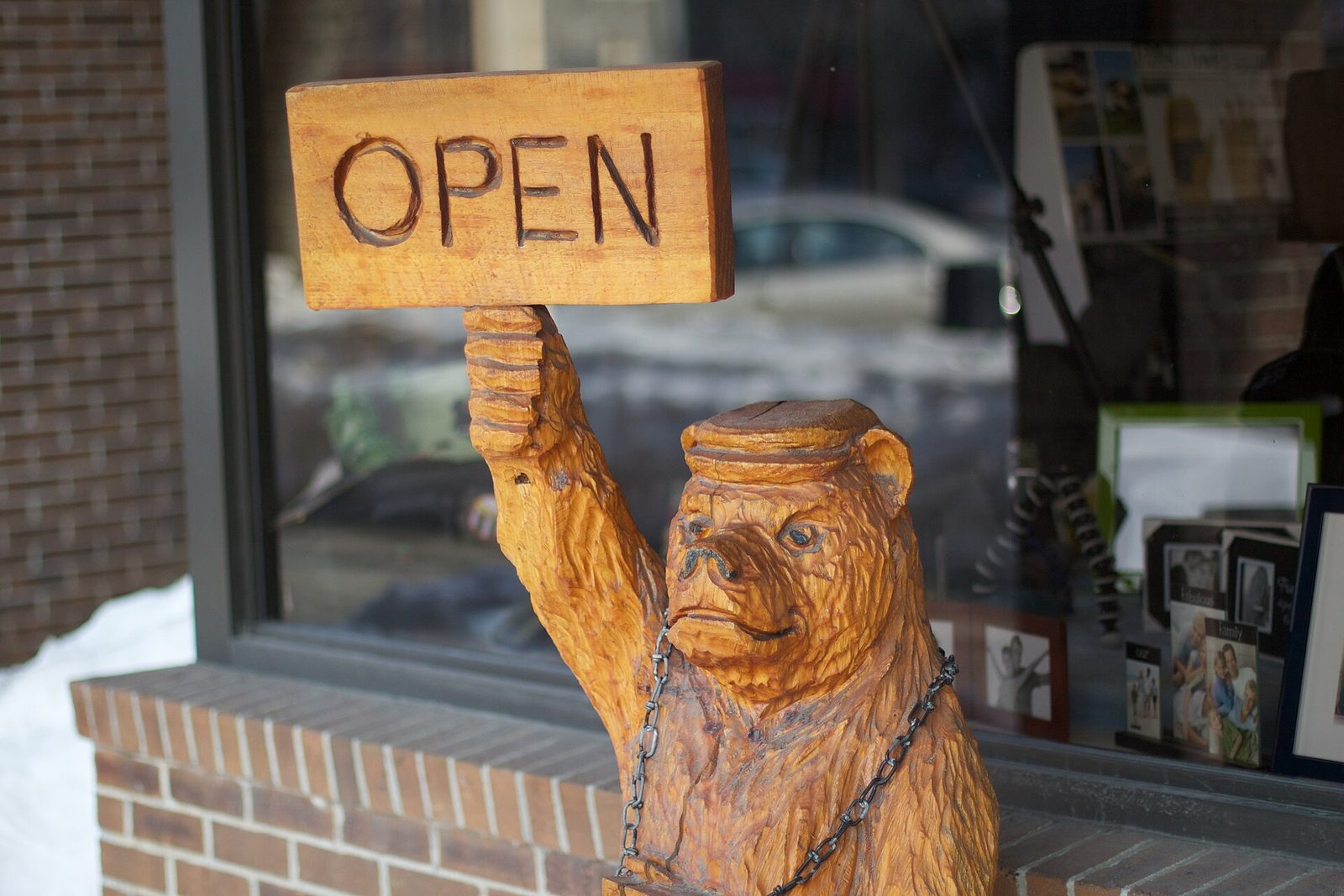 Carved wooden bear holding an OPEN sign beside an independent shop window