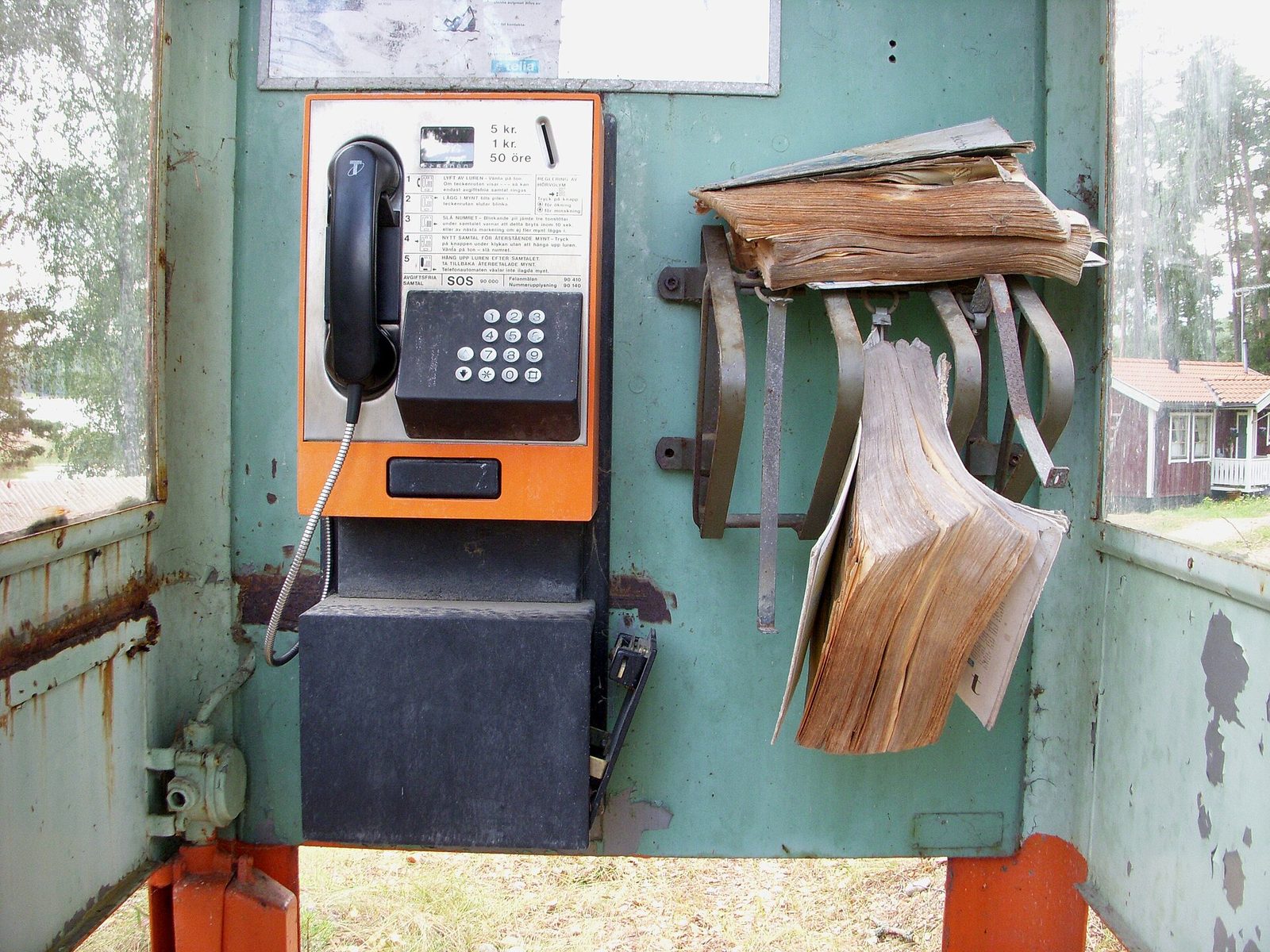 A worn phone book hanging beside a payphone in a weathered outdoor booth