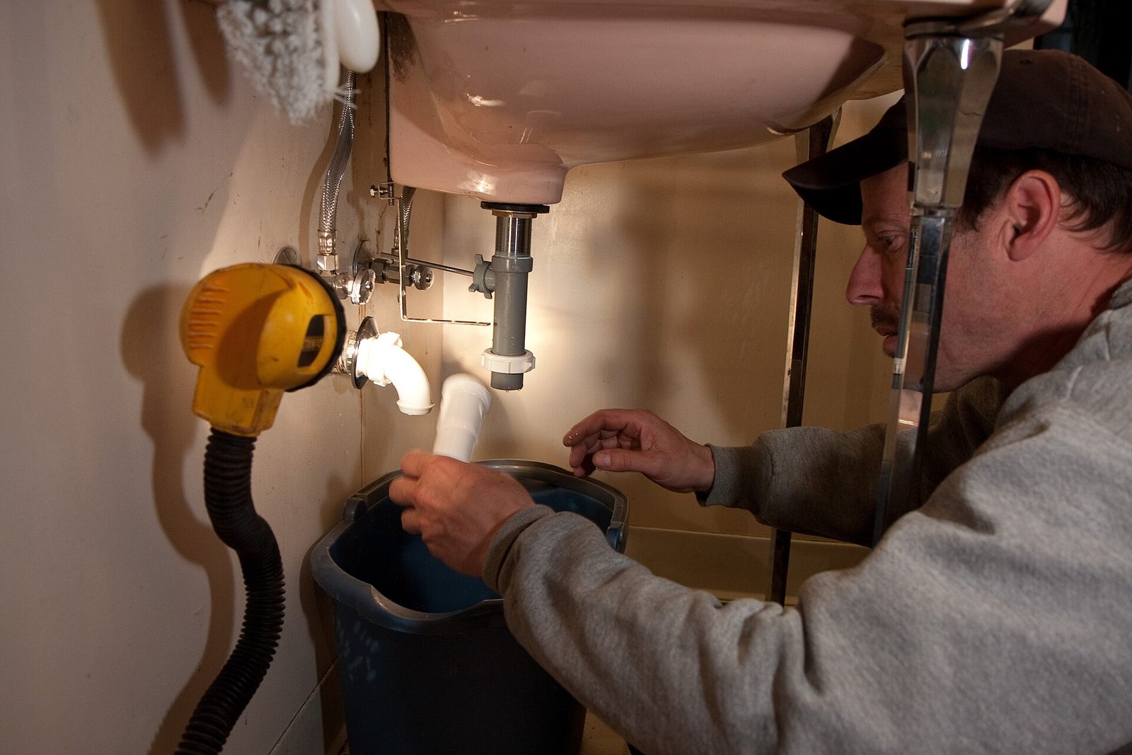 Plumber repairing the pipes under a bathroom sink in a home