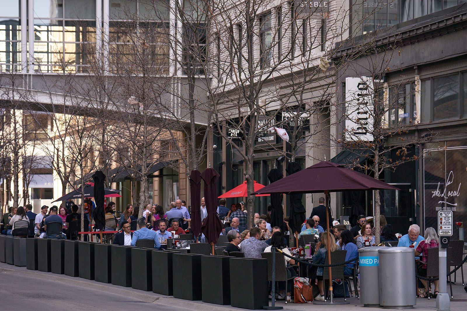Busy downtown restaurant patios with diners at outdoor tables under umbrellas